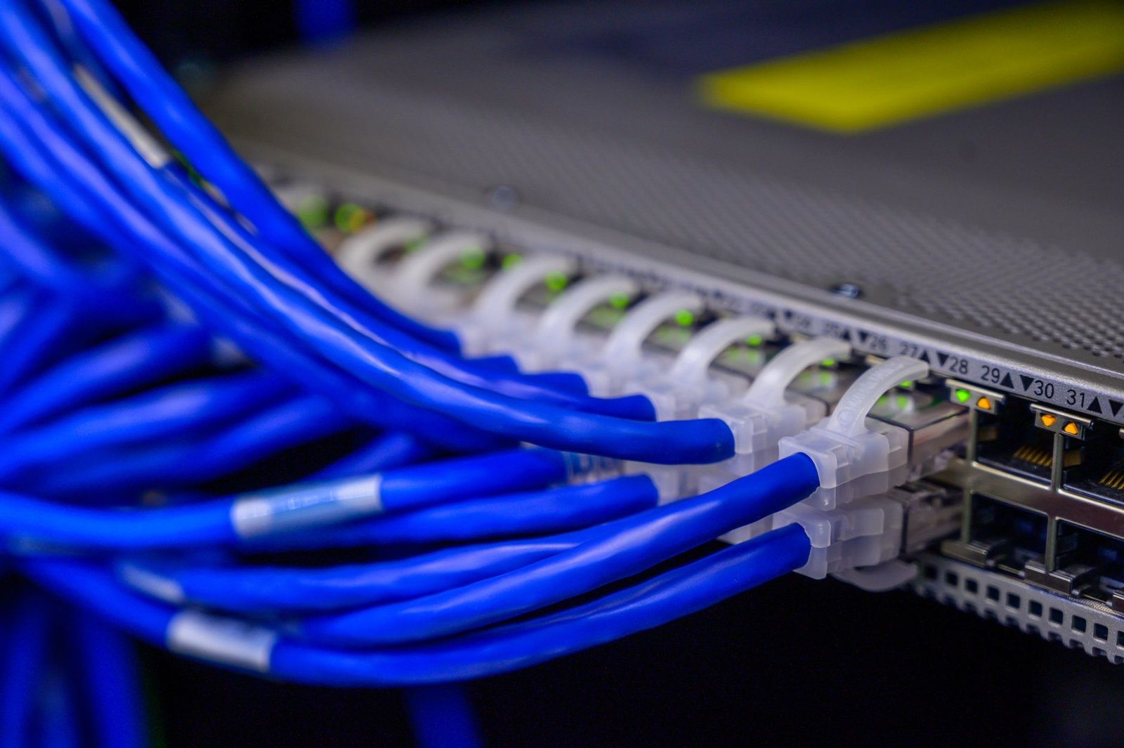 Network engineer configuring a stack of data center spine-leaf switches with fiber optic cables, large server room