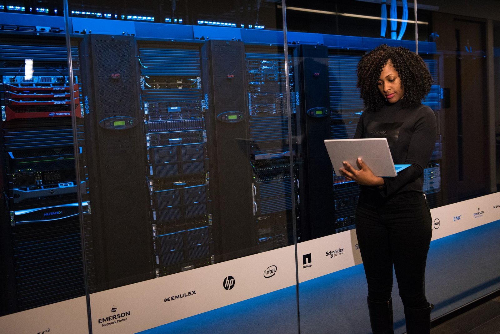 A data center engineer in a blue uniform working on a server rack with fiber optic cables and a glowing LED panel