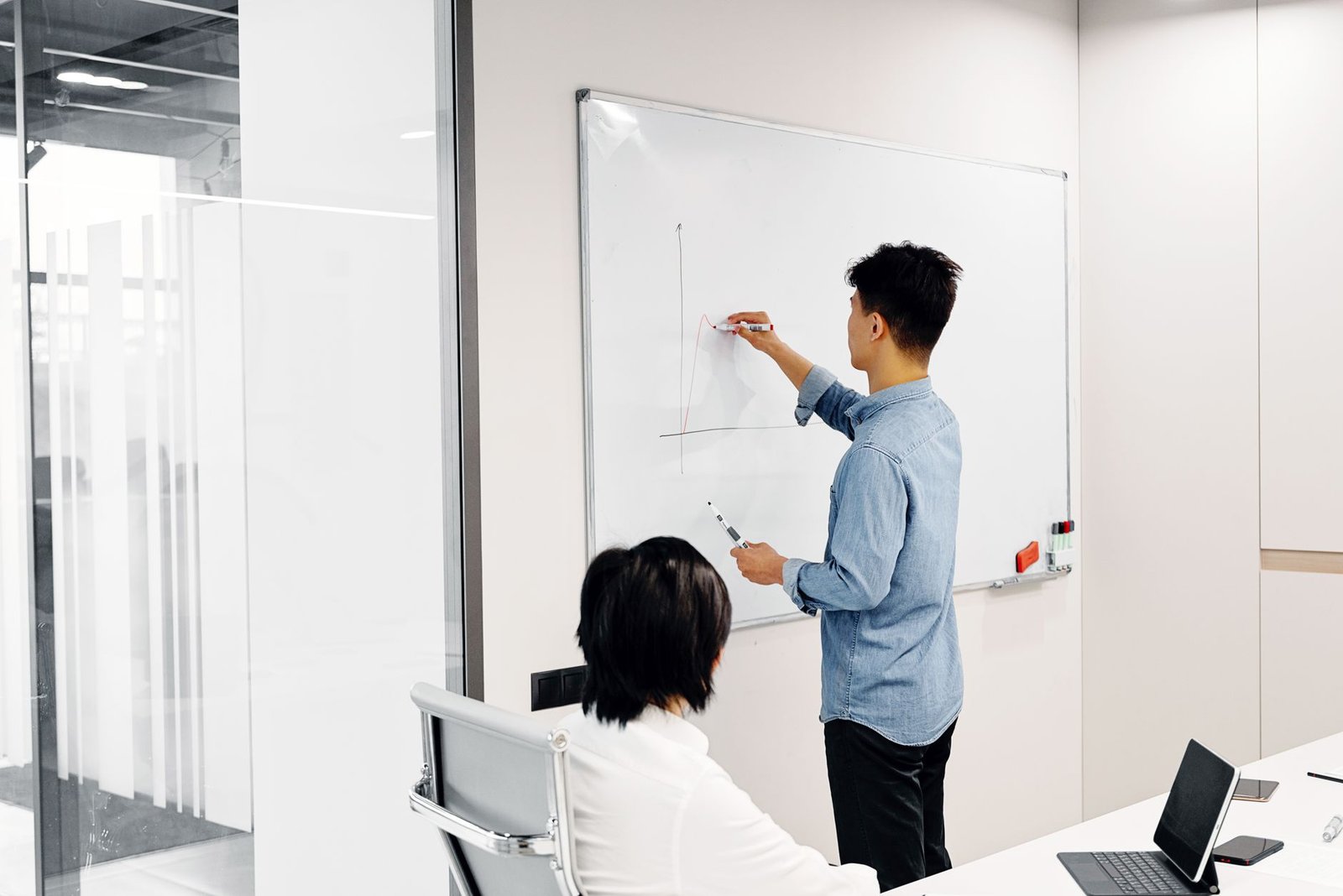 A diverse group of executives around a conference table reviewing an AI value chain diagram on a whiteboard, with data, model, and dollar signs connected