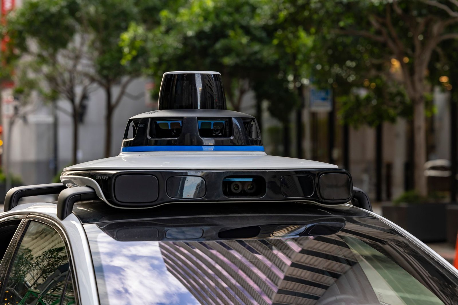 Close-up of a LIDAR sensor mounted on an autonomous test vehicle roof, with out-of-focus car body and highway in the background