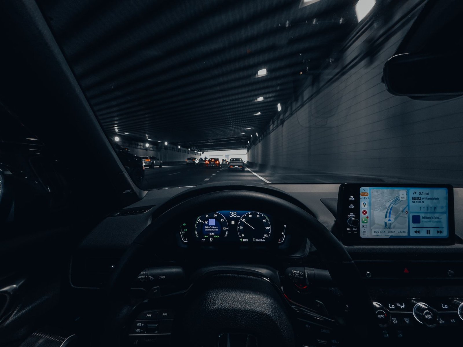 Silhouetted autonomous vehicle driving on a highway at dusk with lidar sensor visible on roof, sensor data visualization overlay on windshield