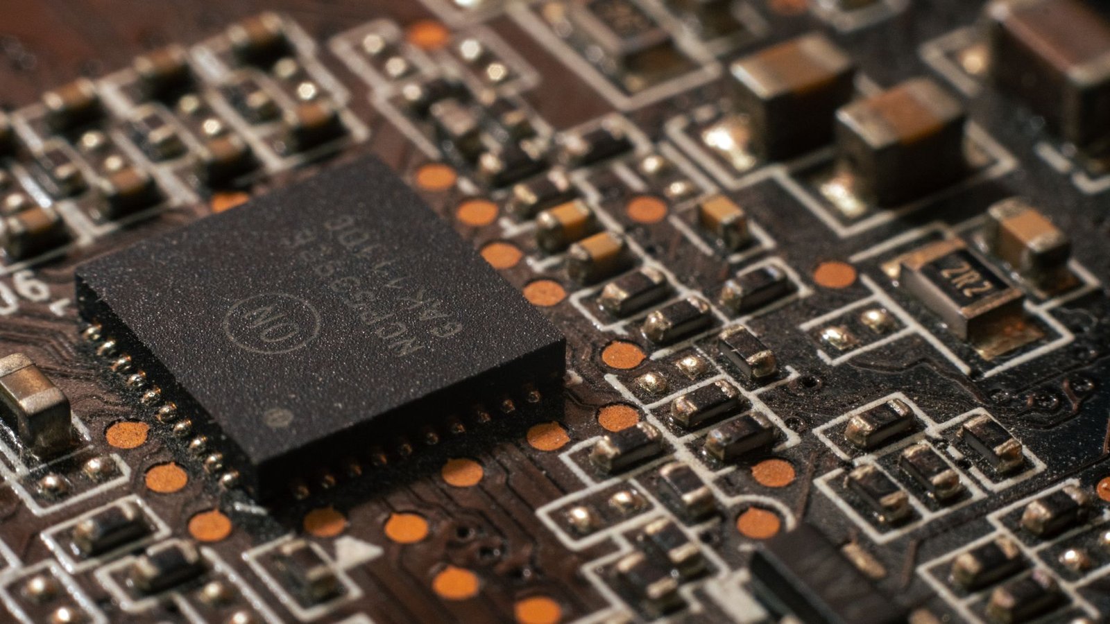 Close‑up of a complex custom AI chip on a green circuit board, surrounded by capacitors and small components, held by an engineer in a clean‑room environment
